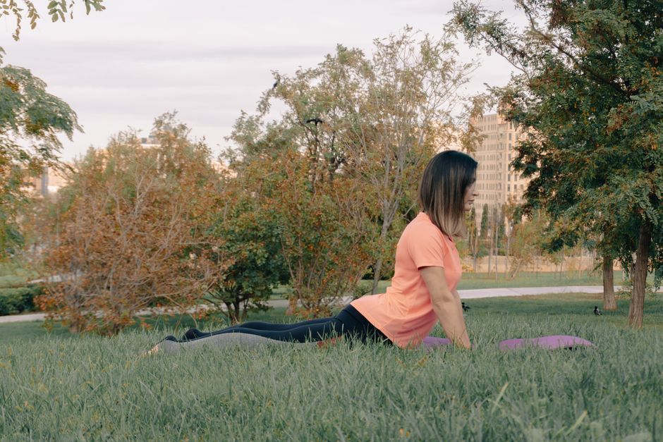 Adult woman performing yoga exercise outdoors in a peaceful park setting, surrounded by greenery.