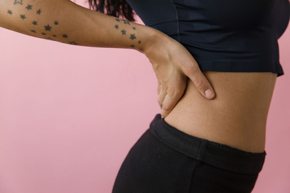 Side view of a tattooed hand on hip against a pink background in a studio setting.