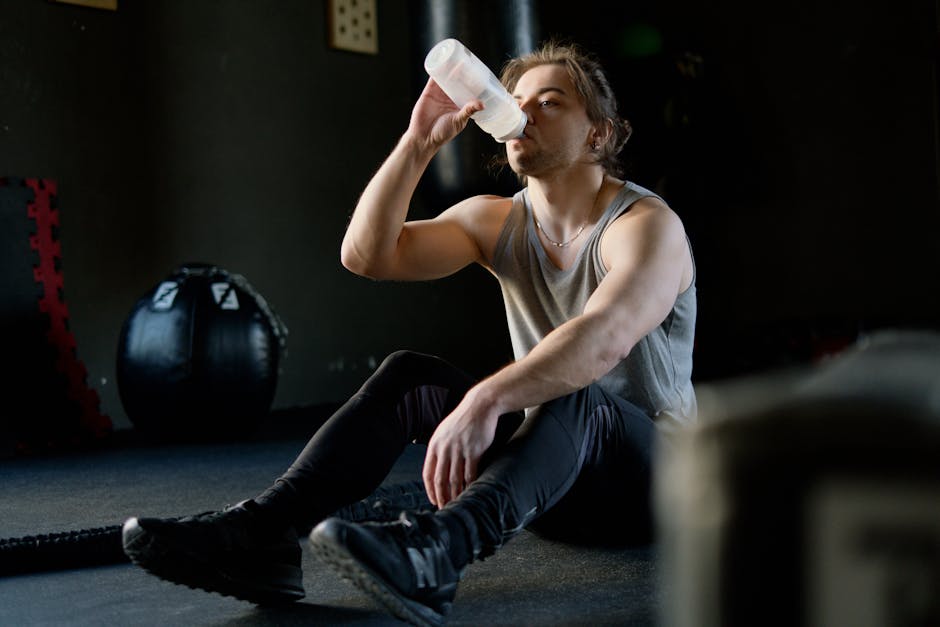 An athletic man in a gym taking a break and drinking water post workout for hydration.