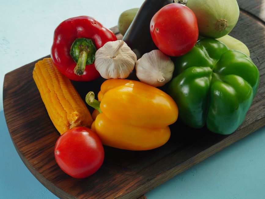Vibrant assortment of fresh vegetables including peppers, tomatoes, and garlic on a wooden board.