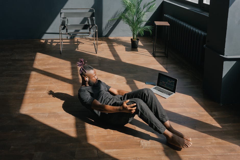 Man doing a workout indoors next to a laptop showing graphs, in a sunlit room.