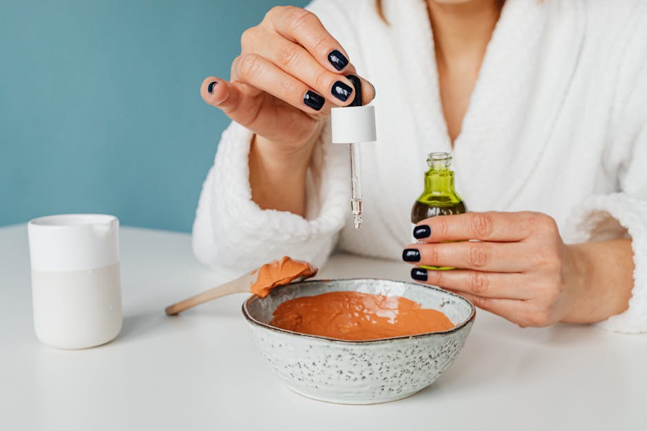 A woman in a bathrobe mixing ingredients for a DIY skincare mask using a pipette.