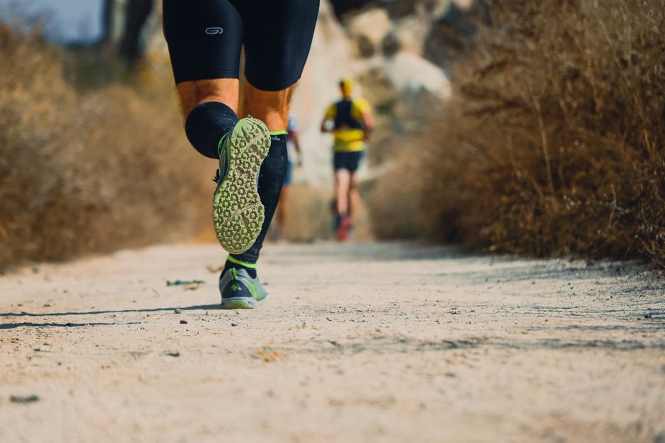 Close-up of runners on a trail, focusing on athletic legs and textured shoes.