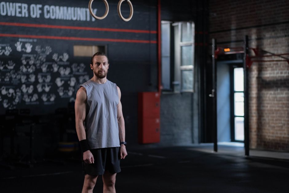 Muscular man standing in a gym with gymnastic rings, showcasing fitness and strength.