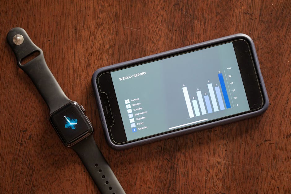 Close-up of a smartphone and smartwatch displaying a weekly report on a wooden table.