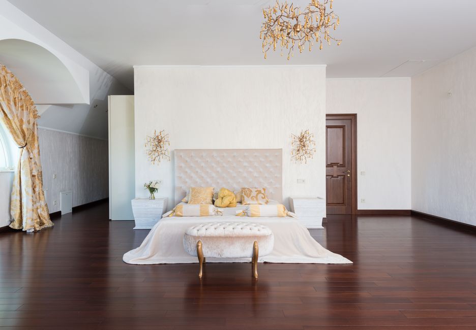 Interior of spacious light bedroom with bed bench at queen size bed with soft headboard with golden bras and chandelier