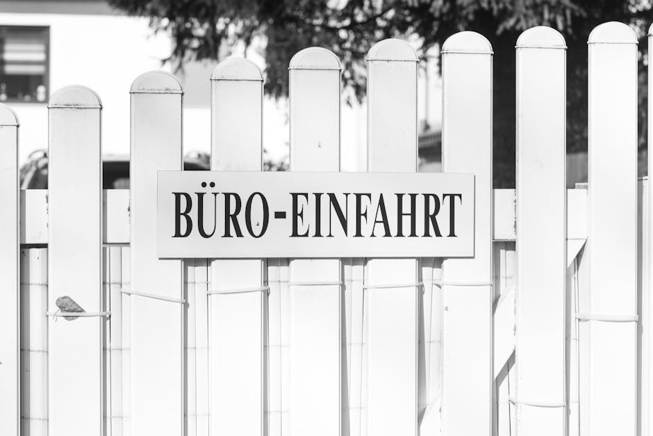 Black and white photo of an office entrance sign on a white picket fence with a tranquil setting.