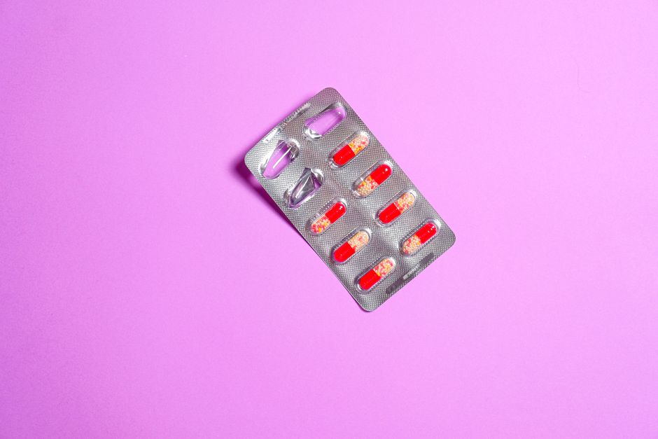 Close-up of a blister pack containing red capsules on a vibrant purple background.