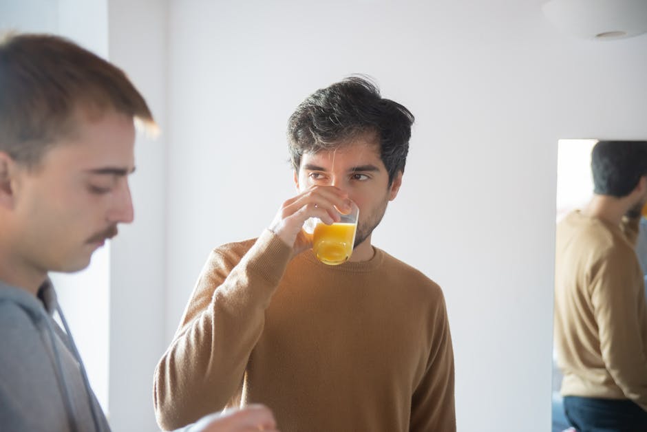 Two men enjoying a relaxed moment at home, drinking juice and reflecting on their relationship.