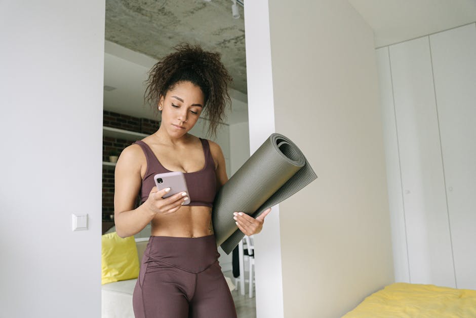 Young woman in activewear holding yoga mat and smartphone, preparing for a home workout.